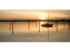 Martha’s Vineyard Wide by Schiffer Publishing, Ltd. captures a sailboat floating at sunset near Martha’s Vineyard, surrounded by wooden posts, with orange and yellow skies reflecting on calm waters and silhouettes of trees and buildings on the horizon.