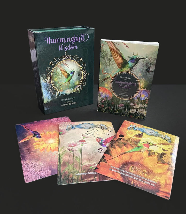 The Hummingbird Wisdom Oracle Cards by Schiffer Publishing, Ltd. are shown in a boxed set with illustrated cards and a guidebook featuring colorful hummingbirds, flowers, and nature scenes arranged on a black surface.