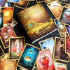 A deck of vibrant Lenormand of Enchantment cards by Schiffer Publishing, Ltd. is spread out with its guidebook, showing animals, flowers, fantasy scenes, and symbols on a dark surface.