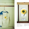 A white sailor-style shirt with blue trim, adorned by a yellow ranunculus, exemplifies wearable plant art. Nearby is "The Herbarium of Fabric Flowers" by Schiffer Publishing, Ltd., echoing the theme of herbarium fabric projects.