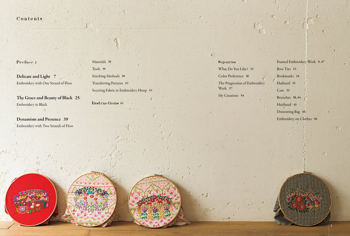 Four colorful hoops with detailed botanical embroidery from Schiffer Publishing, Ltd.’s "Embroidery Garden" rest on wood before a beige wall. Above, a contents page lists sections and page numbers, inspired by Yanase Rei’s artistry.