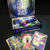 An open box of Magical Dimensions Oracle Cards and Activators by Schiffer Publishing, Ltd. reveals mystical, colorful cards: one with a butterfly, one titled ADVENTURE showing a woman in pink, and one titled CELESTIAL ASSISTANCE with an angel.