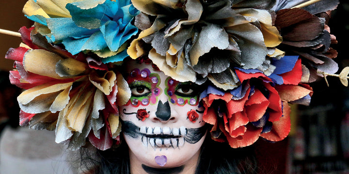 A person with a colorful Día de los Muertos skull face paint and vibrant paper flower crown, featured in "San Miguel de Allende" by Schiffer Publishing, Ltd.—a photo book celebrating this lively UNESCO World Heritage Site.