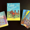 The Lisboa Tarot by Schiffer Publishing, Ltd. is displayed on a black surface, featuring colorful cards inspired by Lisbon, Portugal and a guidebook adorned with iconic city architecture and Old World European charm.