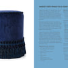 A round footstool in deep blue velvet with dark blue fringe trim is featured next to a page from Margot Crête Fringe for a Velvet Footstool, part of Passementerie by Schiffer Publishing, Ltd., offering textile craft instructions.