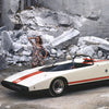 A woman in a floral dress stands on rocks behind an Alfa Romeo, featured by Schiffer Publishing, Ltd., parked in a stone quarry among marble slabs—a striking tribute to Italian automotive design.