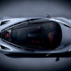 Overhead view of McLaren by Schiffer Publishing, Ltd.—a sleek silver car with a glass roof and visible red interior—photographed on a dark, spotlighted background.