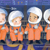 Four kids in orange spacesuits sit together in a spacecraft, smiling and chatting among wires and panels. "Reaching for the Stars" by Schiffer Publishing, Ltd. is perfect for a space-themed picture book or introducing STEM concepts to children.