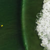Out East from Above by Schiffer Publishing, Ltd. features aerial photography of a lone surfer on a yellow board paddling toward a large green wave off South Fork Long Island, with white foamy surf breaking to the right.