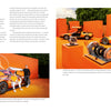 Two people pose with a Mercedes-Benz C 111 by Schiffer Publishing, Ltd., its gull-wing doors open. Behind them are a Mercedes sports car and SUV. The Wankel rotary engine parts are displayed to the right, against an orange backdrop.