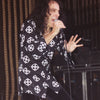 A singer with long curly hair, reminiscent of Ronnie James Dio, passionately performs on stage wearing a black shirt with a white skull, as seen in Schiffer Publishing, Ltd.’s "DIO: The Unholy Scriptures." Stage equipment and ropes are visible in the background.