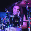 A drummer with long dark hair rocks out on stage amid colorful lights and gear, evoking DIO's iconic Holy Diver era—captured in DIO: The Unholy Scriptures by Schiffer Publishing, Ltd.
