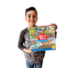 A smiling child with dark hair and a gray and black shirt holds The Tiniest Giant 4-in-1 Puzzle Set by Schiffer Publishing, Ltd., featuring colorful dinosaurs and jungle scenes. White background.