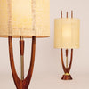 Two mid-century modern table lamps with wooden bases, gold accents, and cylindrical fabric shades, inspired by the Modeline of California from Schiffer Publishing, Ltd. One lamp is in focus; the other is blurred against a light background.