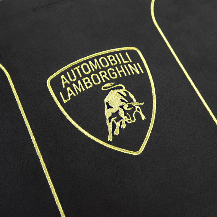 Close-up of the Lamborghini logo with a gold bull and “Automobili Lamborghini” embroidered on black fabric, showcasing the elegance celebrated in every copy of Automobili Lamborghini Special Edition by Schiffer Publishing, Ltd.