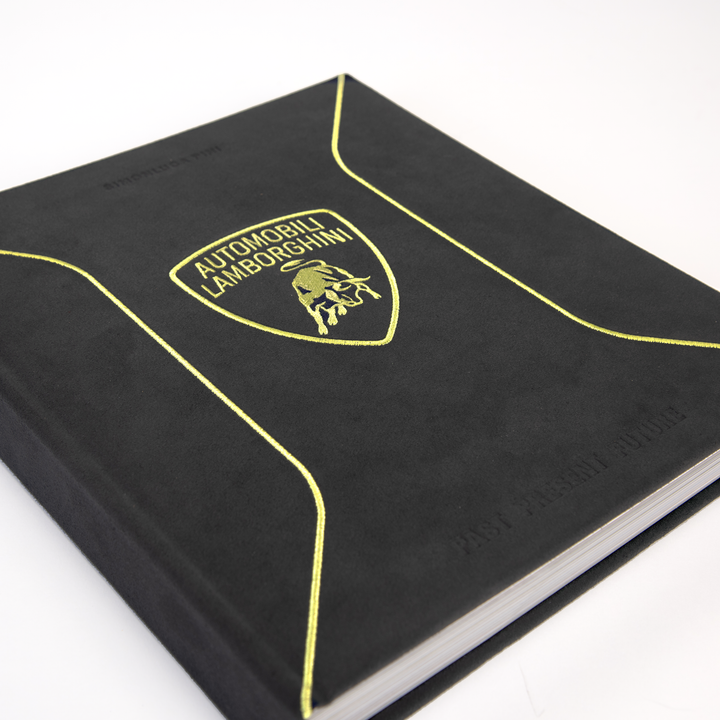The Automobili Lamborghini Special Edition by Schiffer Publishing, Ltd. is a black book with yellow trim, suede-like cover, embossed lower-right text, and the iconic bull logo—perfect for luxury sportscar enthusiasts.