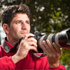 A man in a red jacket holds a camera outdoors, evoking the adventurous vibe of Pacific Northwest beverage culture showcased in "Drinkin' Up the Pacific Northwest" by Schiffer Publishing, Ltd.