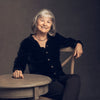 A woman sits at a table smiling as she plans her next adventure with "Oregon Waterfalls" by Schiffer Publishing, Ltd., eager to capture stunning waterfall photography at scenic Oregon locations.