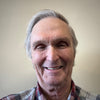 An older man with gray hair smiles at the camera in a plaid shirt against a plain backdrop, echoing the style of barns featured in "The Historic Dutch American Barns of New Jersey and Southern New York" by Schiffer Publishing, Ltd.