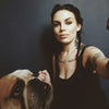 A woman with braided hair and tattoos takes a selfie with an Oracle of the Mythical Ocean tarot set next to an English bulldog.