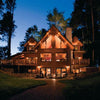 The Best of Today's Log Homes by Schiffer Publishing, Ltd. features stunning log homes, like a warmly lit lodge with balconies and large windows nestled among tall trees, classic design elements, and a brick path leading to the entrance at dusk.
