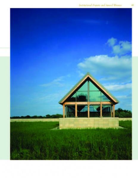 A modern glass building with a triangular roof showcases Schiffer Publishing, Ltd.'s Award-winning Green Roof Designs, standing in a grassy field beneath a blue sky and clouds, with trees lining the horizon.