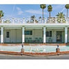 Small Dreams by Schiffer Publishing, Ltd. features a white, single-story motel with columns, a balcony, and palm trees, plus a circular fountain with statues shining under a clear sky, reflecting Palm Springs style.