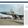 Two MiG-29 air-superiority fighters, featured in "The MiG-29" by Schiffer Publishing, Ltd., are parked on an airfield under a clear sky, with a building and trees visible in the distance. One fighter stands in the foreground and another in the background.