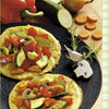 Two omelets with sautéed vegetables, including zucchini, are presented on a black plate surrounded by fresh veggies—perfect inspiration from Schiffer Publishing, Ltd.'s Squash & Zucchini. Fresh vegetables adorn the wooden surface around the plate.