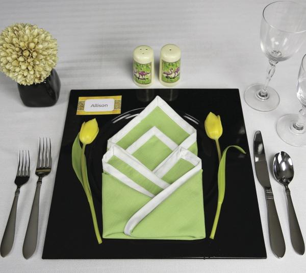 Set a chic table with silverware, glasses, a black plate, and a folded green and white napkin—framed by yellow tulips—as featured in Schiffer Publishing, Ltd.'s Creative Napkins and Table Settings. A name card and yellow arrangement complete the look.