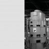 Black-and-white photo from The Neutron's Long Shadow (Schiffer Publishing, Ltd.) shows two large machines labeled "12" and "14," tied to the Manhattan Project, with control panels and pipes inside a spacious factory. Left side features a small text block.