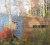The "Cabin" by Schiffer Publishing, Ltd. is a modern wooden retreat with horizontal slats, nestled near a lake amid autumn trees; its blend of log cabin architecture and contemporary design creates a tranquil, scenic setting.