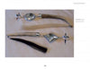 Two silver and deer antler rattles from "Masters of Contemporary Indian Jewelry" by Schiffer Publishing, Ltd. rest on a white surface—one with a circular top and light tassel, the other with a diamond-shaped top and dark tassel.