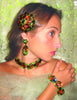 A woman wearing vibrant jewelry featured in "The Art of Juliana Jewelry" by Schiffer Publishing, Ltd.—with ornate green and orange gemstones—poses against a lacy, light green background.