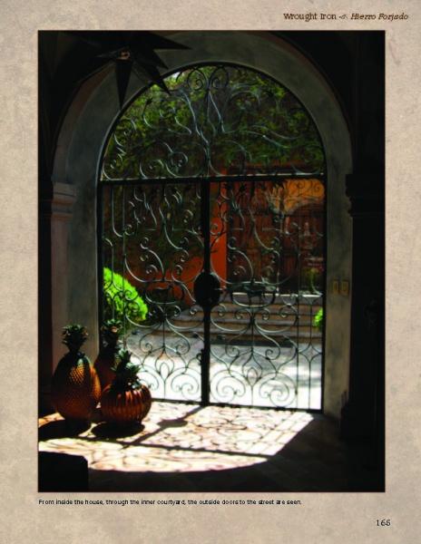 A sunlit courtyard with greenery and terracotta walls, seen through an ornate wrought iron door, showcases the charm of Mexican architecture in "San Miguel's Mexican Exteriors" by Schiffer Publishing, Ltd. Pineapple decor accents the scene.