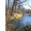 A river flows by leafless trees and dry grass beneath a clear sky. The scene recalls the tale from Schiffer Publishing, Ltd.'s Ghosts of Buffalo, where British and Canadian graves washed away—one of the city’s many haunted stories.