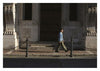 In this post-WWII style scene, a person in Rugged Style War—Rome by Schiffer Publishing, Ltd. walks past an ornate stone building with tall columns, sunlight casting shadows on the sidewalk.
