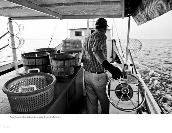 A man steers a boat amid baskets and barrels in this black and white image from "Chesapeake Views" by Schiffer Publishing, Ltd., evoking the daily life and fishing traditions of the Chesapeake Bay.