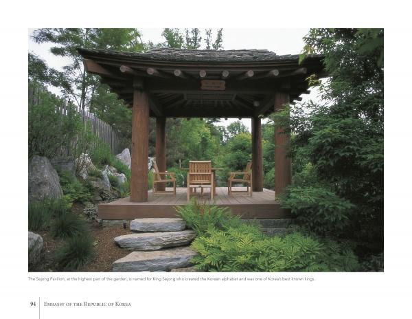 Inspired by "Diplomatic Gardens of Washington" by Schiffer Publishing, Ltd., a wooden pavilion with a tiled roof sits amid lush greenery and rocks, sheltering four wooden chairs and a small table in a private garden.