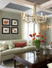An inviting living room with a light sofa, red pillow, and vase of orange tulips on a polished table, inspired by "Showhouses 3" from Schiffer Publishing, Ltd., features wall art and a crystal chandelier overhead.