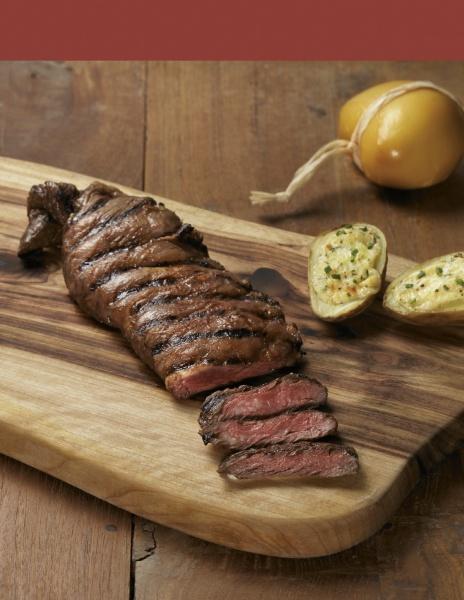 A juicy grilled steak from "Pure Steak" by Schiffer Publishing, Ltd., sliced to show a pink center, served with baked potatoes and yellow cheese—ideal inspiration for steak cookbook fans or beef cut enthusiasts.