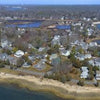 Aerial view of a coastal neighborhood on a peninsula with houses, trees, roads, and shoreline under a clear sky—featured in "Cape Cod and the Islands" by Schiffer Publishing, Ltd.