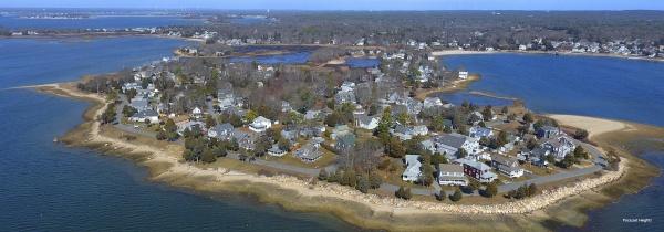 Aerial view of a coastal neighborhood on a peninsula with houses, trees, roads, and shoreline under a clear sky—featured in "Cape Cod and the Islands" by Schiffer Publishing, Ltd.
