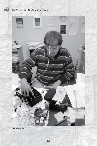 A man sits at a cluttered desk with wires attached to his head, researching Missouri ghost stories with "Paranormal Missouri" by Schiffer Publishing, Ltd. Caption: Me feeling silly investigating local hauntings.