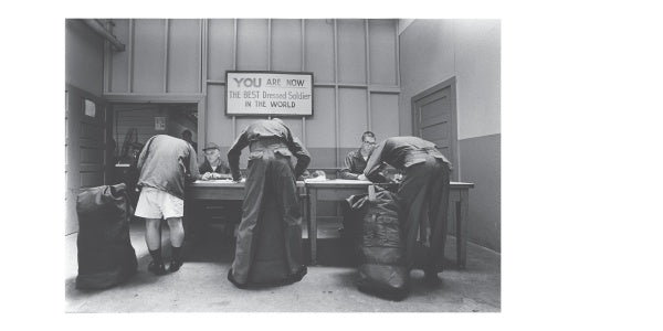 In "Grunts" by Schiffer Publishing, Ltd., four soldiers with duffel bags stand at a table while two men sit behind it, echoing classic U.S. Army draft scenes in photojournalistic essay style.