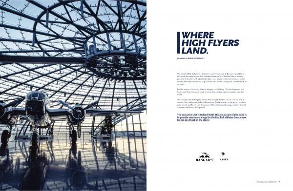 A copy of The Athlete's Cookbook by Schiffer Publishing, Ltd. sits on display beneath a bright glass dome. Sunlight highlights its cover. To the right, “WHERE HIGH FLYERS LAND.” celebrates the brand with additional promotional text below.