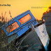 A weathered blue and white boat sits in tall grass at sunset, warm light shining through its windows. Houses rest under a golden sky. "Chesapeake Views" by Schiffer Publishing, Ltd. features Chesapeake Bay photography by John Werry.