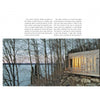 The Cabin by Schiffer Publishing, Ltd. is a modern wood-and-glass cabin inspired by log cabin design, featuring warm lighting and set among leafless trees on a rocky lakeshore overlooking calm water under an overcast sky.