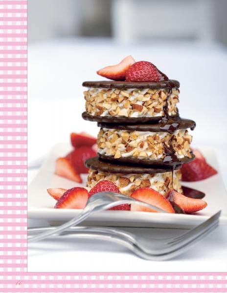 Three stacked ice cream sandwiches with nuts, chocolate sauce, and fresh strawberry slices from Asparagus & Strawberries by Schiffer Publishing, Ltd., served on a white plate—an irresistible treat for strawberry lovers. Two forks rest in front.