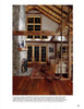 A cozy living room inspired by "Barn Again" from Schiffer Publishing, Ltd., with vaulted ceilings, wooden beams, a stone fireplace, wood floor, rocking chairs, and a rug. French doors and warm lighting complete the inviting atmosphere.
